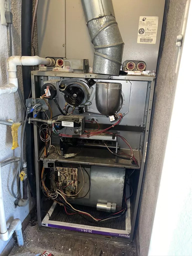Open view of a gas furnace showing internal components including blower motor, circuit board, and burners during HVAC maintenance
