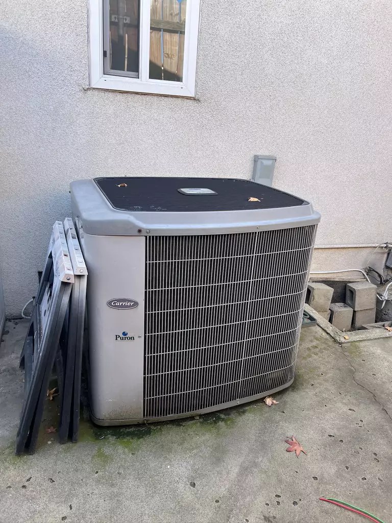 Exterior view of a Carrier Puron air conditioning unit on a residential property, set up near a wall and windows