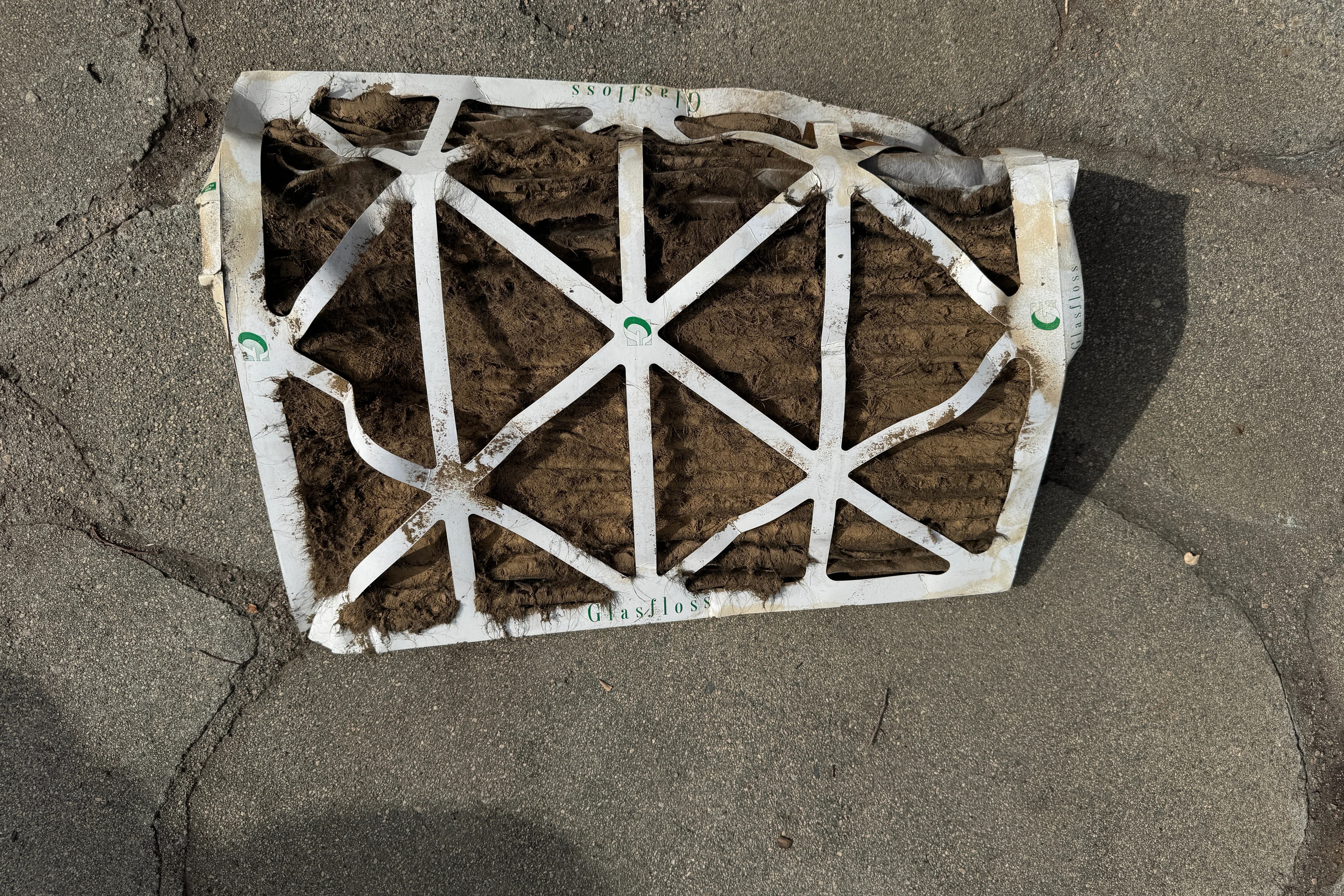 Collapsed and heavily clogged HVAC air filter lying on concrete, showing buildup of dust and debris due to lack of replacement
